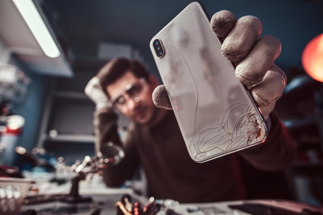 Técnico electrónico mostrando un teléfono inteligente moderno con el cuerpo roto